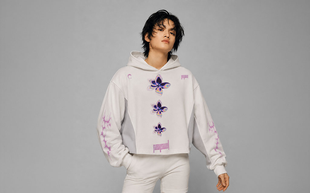 Close-up front view of model wearing a white cropped hoodie with three purple and gold butterfly graphics down the chest and Arabic calligraphy print at the hem, matching purple vein sleeve prints, grey side panels — streetwear brand hoodie collection.