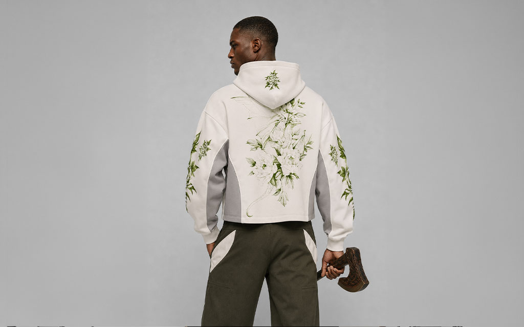 Back view of model wearing a white cropped hoodie with a green floral dragon graphic across the back and matching botanical sleeve prints, grey side panels, paired with olive cargo pants — streetwear brand hoodie collection.